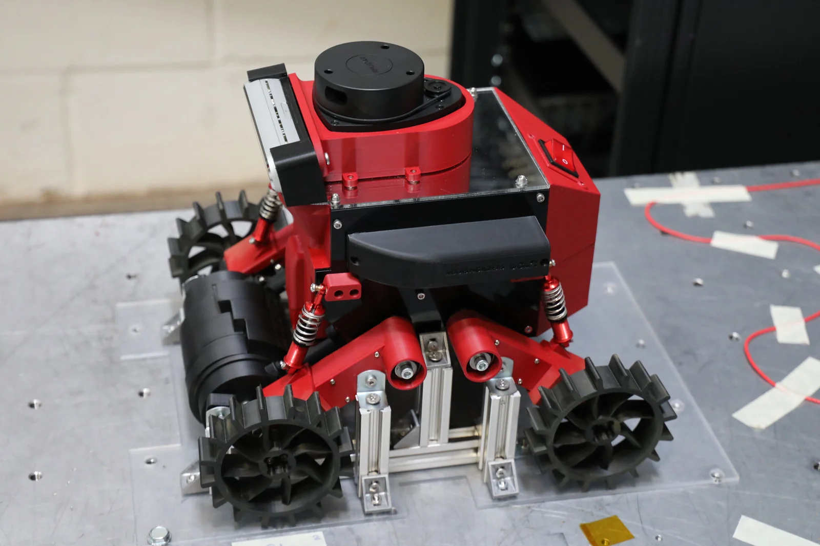 Red and black rover on a support stand, showing its wheels, suspension and LiDAR.